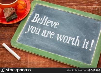 Believe you are worth it - Motivational advice on a slate blackboard with chalk and cup of tea