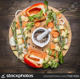 bell peppers, various unground pepper, chopped carrots, potatoes and herbs on a cutting board on wooden rustic background top view
