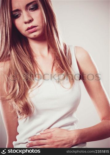 Bellyache, indigestion or menstruation. Young woman suffering from stomach pain studio shot on gray