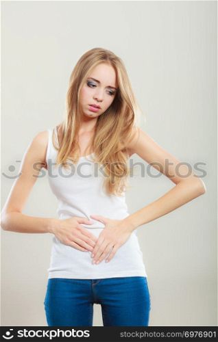 Bellyache, indigestion or menstruation. Young woman suffering from stomach pain studio shot on gray
