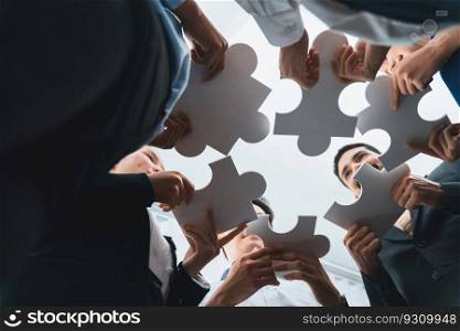 Below view of diverse corporate officer workers collaborate in office connecting puzzle pieces as partnership and teamwork concept. Unity and synergy in business idea by merging jigsaw puzzle. Concord. Diverse corporate officer workers connecting puzzle pieces. Concord