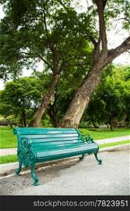Bench under a tree. A seat to rest. Along the corridor. Within the park.