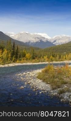 Bend of Snaring River in Jasper National Park, Alberta province, Canada. The park is a UNESCO World Heritage site. Snow on peaks of mountains behind flowing stream. Snaring river is a tributary of Athabasca River.