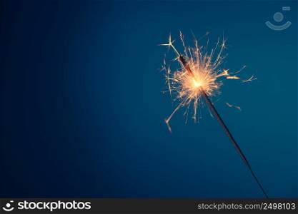 Bengal fire sparkler burning with sparks on blue background