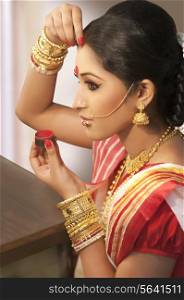 Bengali woman putting sindoor on her forehead