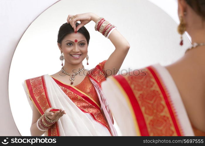 Bengali woman putting sindoor on her forehead