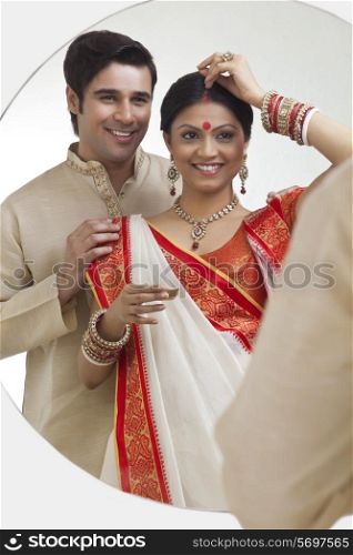 Bengali woman putting sindoor on her forehead while husband watches on