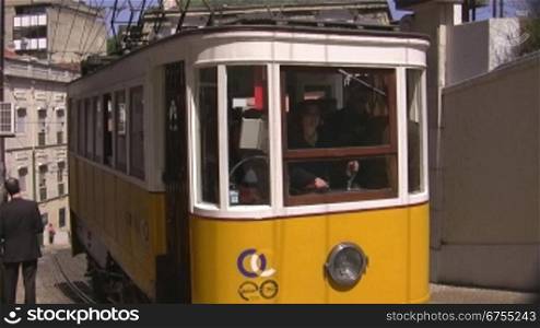 Bergauffahrende gelbe Tram in Lissabon, rechts und links Mauern, dann HSuser.