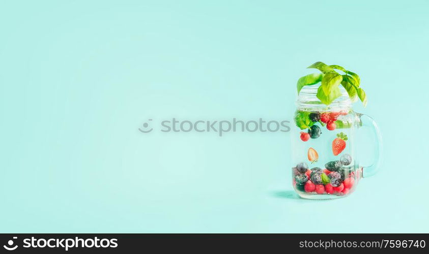 Berries detox fruit infused water in Mason jar flavored with herb leaves on table at sunny turquoise blue background. Summer mood drinks and lifestyle. Healthy background