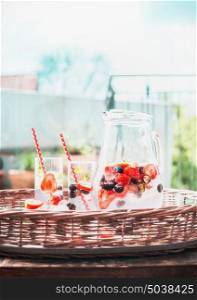 Berries Infused water with ice cubes in jug on tray at outdoor nature background, front view