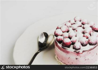 berries toppings round cake with stainless spoon plate against white backdrop