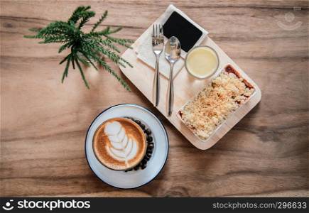 Berry and apple crumble on wood tray with hot latte coffee on wood table. Top view food shot