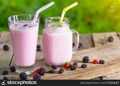 Berry smoothie or yogurt in a jar and a glass with a straw on a wooden table. Berry smoothie or yogurt in jar and glass with straw
