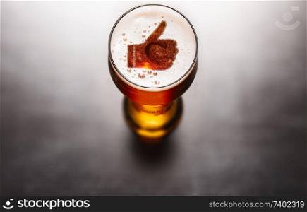 Best beer concept. Thumbs up symbol on beer glass foam on black table, view from above. Best beer concept
