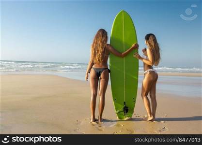 Best friends enjoying the summer, posing with a surfboard on the beach