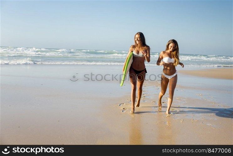 Best friends enjoying the summer, running on the beach with a surfboard