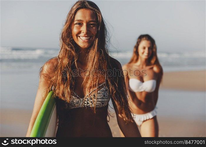 Best friends enjoying the summer, walking on the beach with a surfboard