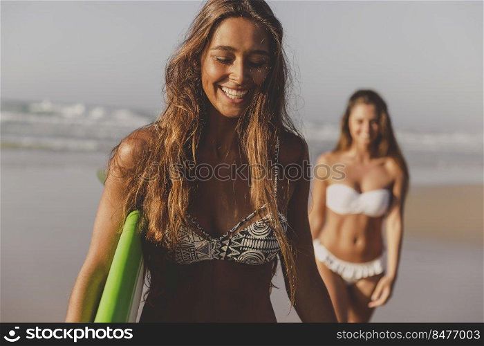 Best friends enjoying the summer, walking on the beach with a surfboard