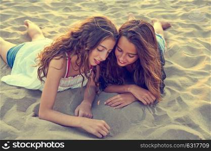 Best friends girls drawing finger on beach sand at summer