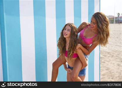 Best friends girls piggyback in summer beach with blue stripes background