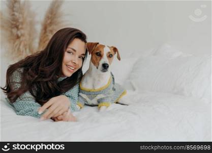 Best friends. Pleased attractive woman lies near jack russell terrier dog, expresses love and care to favorite pet, plays with domestic animal, relax together on white blanket. Animals care concept.