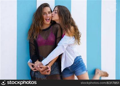 Best friends teen girls happy kiss in a summer blue stripes background