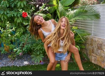 Best friends teen girls piggyback on backyard garden happy smiling