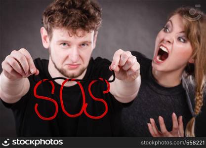 Betrayal and break up in relationship. Young couple arguing and holding red sos word sign symbol. Blonde woman in fury yelling on man. Negative emotions.. Young couple with broken heart and sos word.