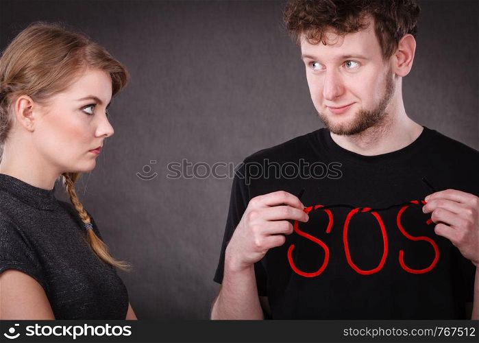 Betrayal and break up in relationship. Young couple with big plaster broken heart and red sos word sign symbol. Negative emotions.. Young couple with broken heart and sos word.