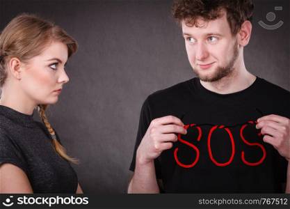 Betrayal and break up in relationship. Young couple with big plaster broken heart and red sos word sign symbol. Negative emotions.. Young couple with broken heart and sos word.
