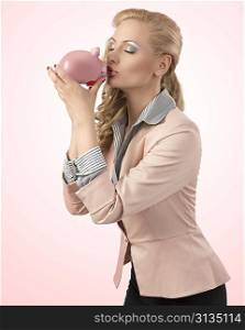 beutiful blonde woman wearing business suit and pretty make-up taking piggybank in the hands and kissinh that