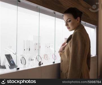 beutiful winter dressed woman , inside a jewellery , looking for some jewel to buy . she is near the lighting shop window.natural ambient light