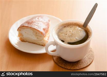Beverage and sweet food. Cup of hot drink coffee and plate with bun with cream dessert on wooden table.