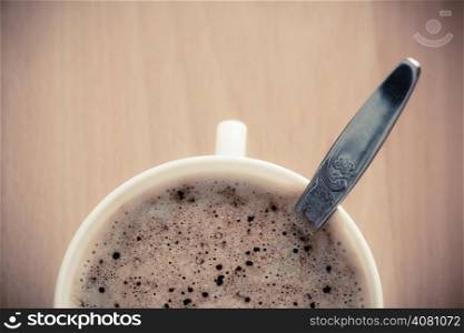 Beverage. Closeup of cup of hot drink coffee cappuccino with froth and teaspoon on wooden table background.