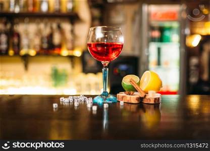 Beverage in glass, lime, lemon, salt and dice on wooden bar counter