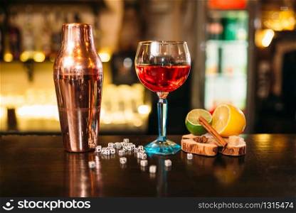 Beverage in glass, shaker, lime, lemon, salt and dice on wooden bar counter