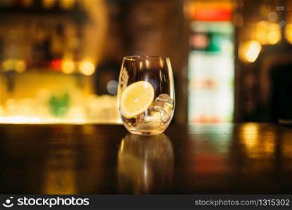 Beverage with slice of lemon and ice cubes on wooden bar counter. Beverage with slice of lemon and ice cubes