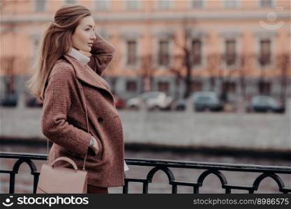 Bfashionable coat, beautiful woman dressed in stylish coat, keeps hand in pocket, focused into distance, has walk at city, thinks bout something, has good rest. People and lifestyle concept.