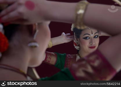 Bharatanatyam dancer getting dressed in front of mirror over black background