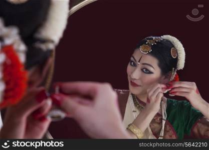 Bharatanatyam dancer wearing earring in front of mirror over black background