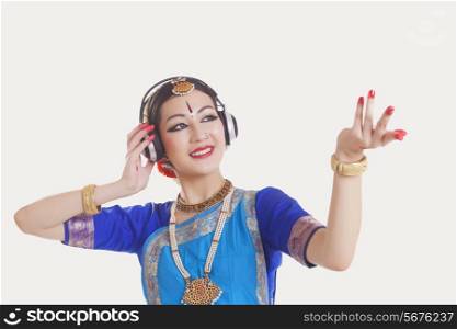 Bharatanatyam dancer wearing headphones while dancing over white background
