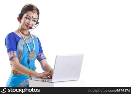 Bharatanatyam dancer wearing headset while using laptop over white background
