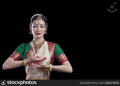 Bharatanatyam dancer with eyes closed performing over black background