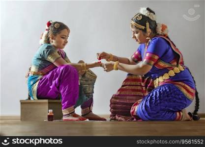Bharatnatyam dancer applying alta on her student’s palms. 