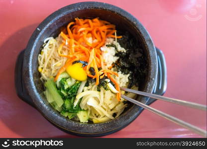 Bibimbap in a heated stone bowl, a signature korean dish with egg and fresh vegetables