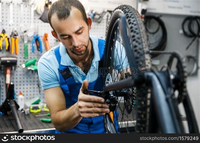 Bicycle assembly in workshop, chain installation. Mechanic in uniform fix problems with cycle, professional bike repairing service. Bicycle assembly in workshop, chain installation