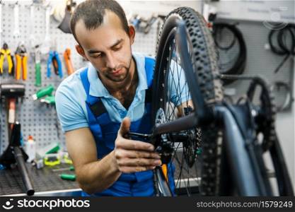 Bicycle assembly in workshop, chain installation. Mechanic in uniform fix problems with cycle, professional bike repairing service. Bicycle assembly in workshop, chain installation