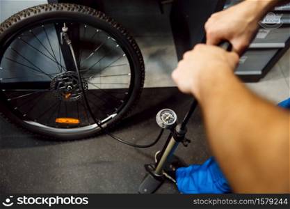 Bicycle assembly in workshop, man inflates the wheel. Mechanic in uniform fix problems with cycle, professional bike repairing service. Bicycle assembly in workshop, man inflates wheel