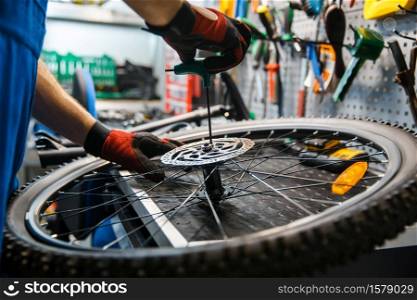 Bicycle assembly in workshop, man installs brake disk. Mechanic in uniform fix problems with cycle, professional bike repairing service. Bicycle assembly in workshop, man installs brake
