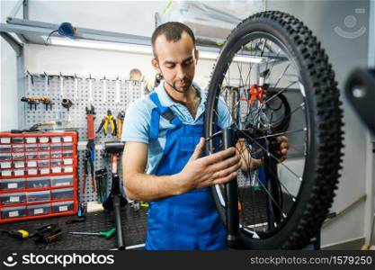 Bicycle assembly in workshop, man setting up a chain. Mechanic in uniform fix problems with cycle, professional bike repairing service. Bicycle assembly in workshop, man setting up chain